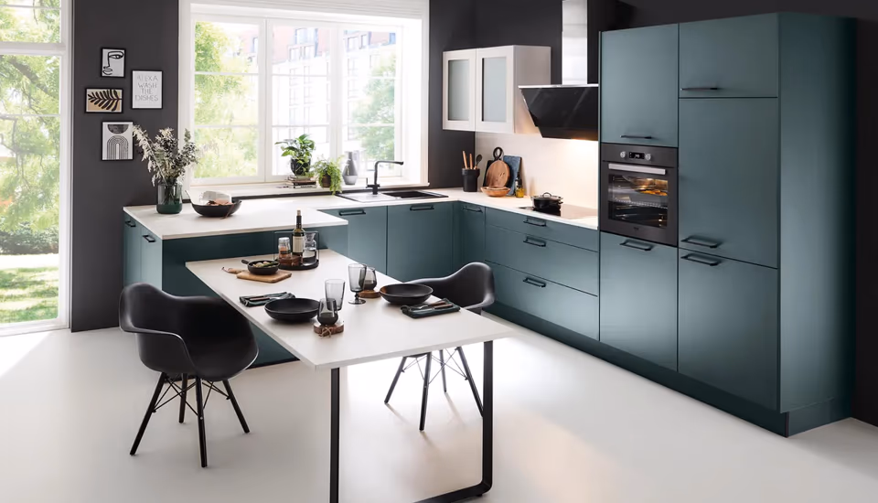 Designorientierte Küche in dunklem Grün mit integriertem Esstisch, großen Fenstern und kontrastreicher Wandgestaltung, ideal für moderne Wohnküchen mit urbanem Charme.